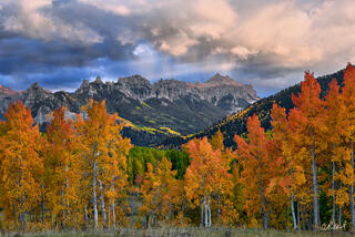 Owl Creek Pass in Colorado framed by brilliant autumn aspens beneath the rugged San Juan Mountains and dramatic storm clouds.