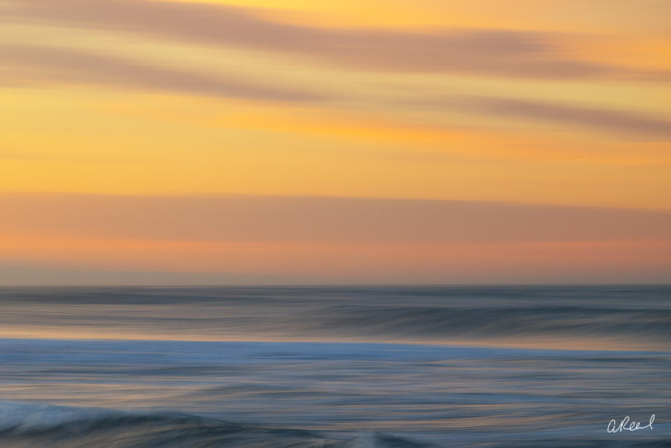 Abstract ocean photography print with soft blue waves beneath a glowing golden, peach and lavender sunset sky.