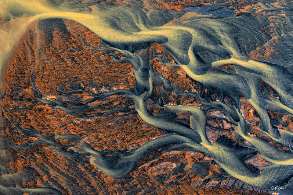 Aerial view of golden braided glacial rivers winding through blue-gray and rust-colored volcanic terrain in Iceland.